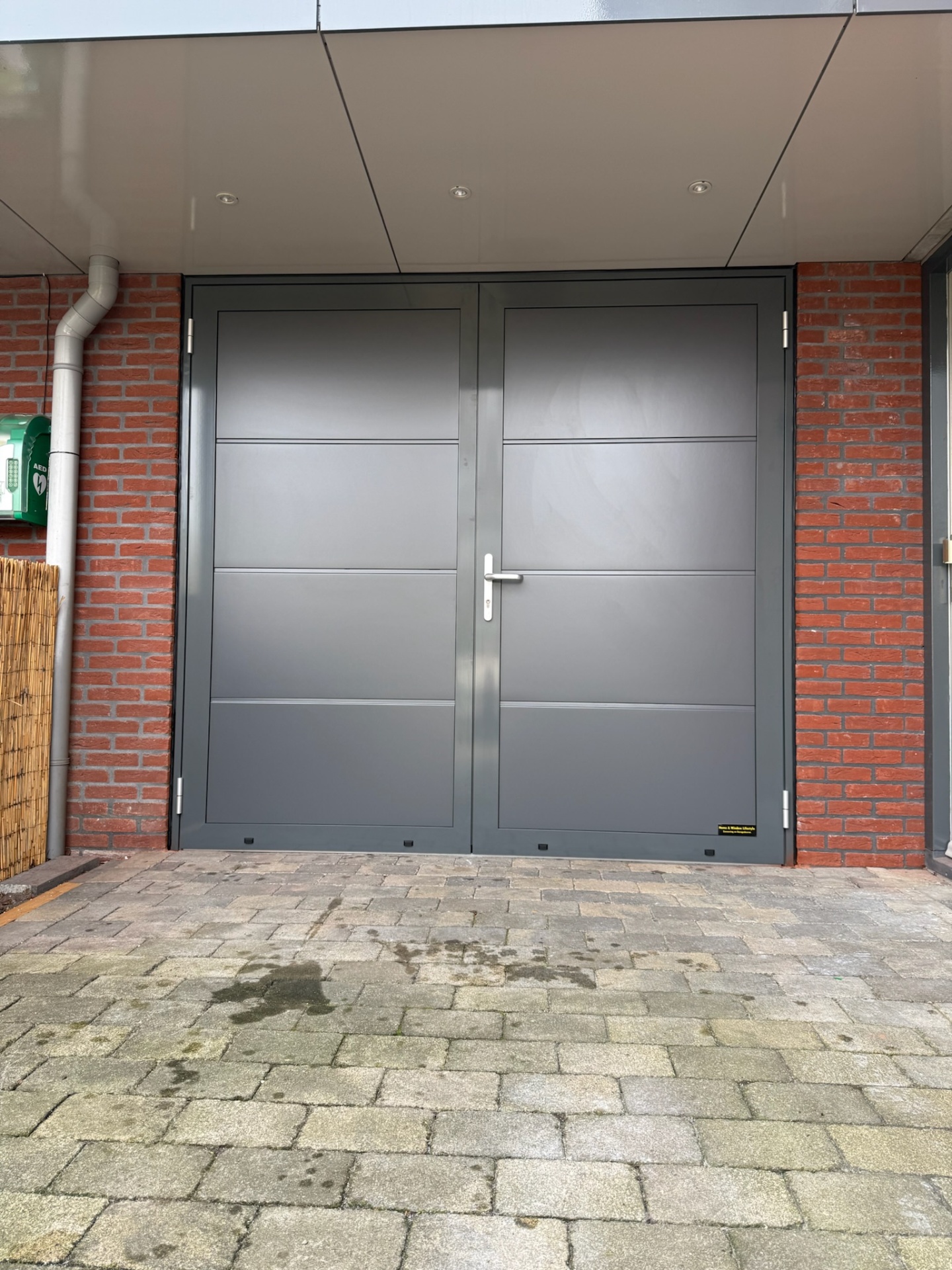 Antraciet garagedeur met horizontale belijning aan rode bakstenen woning