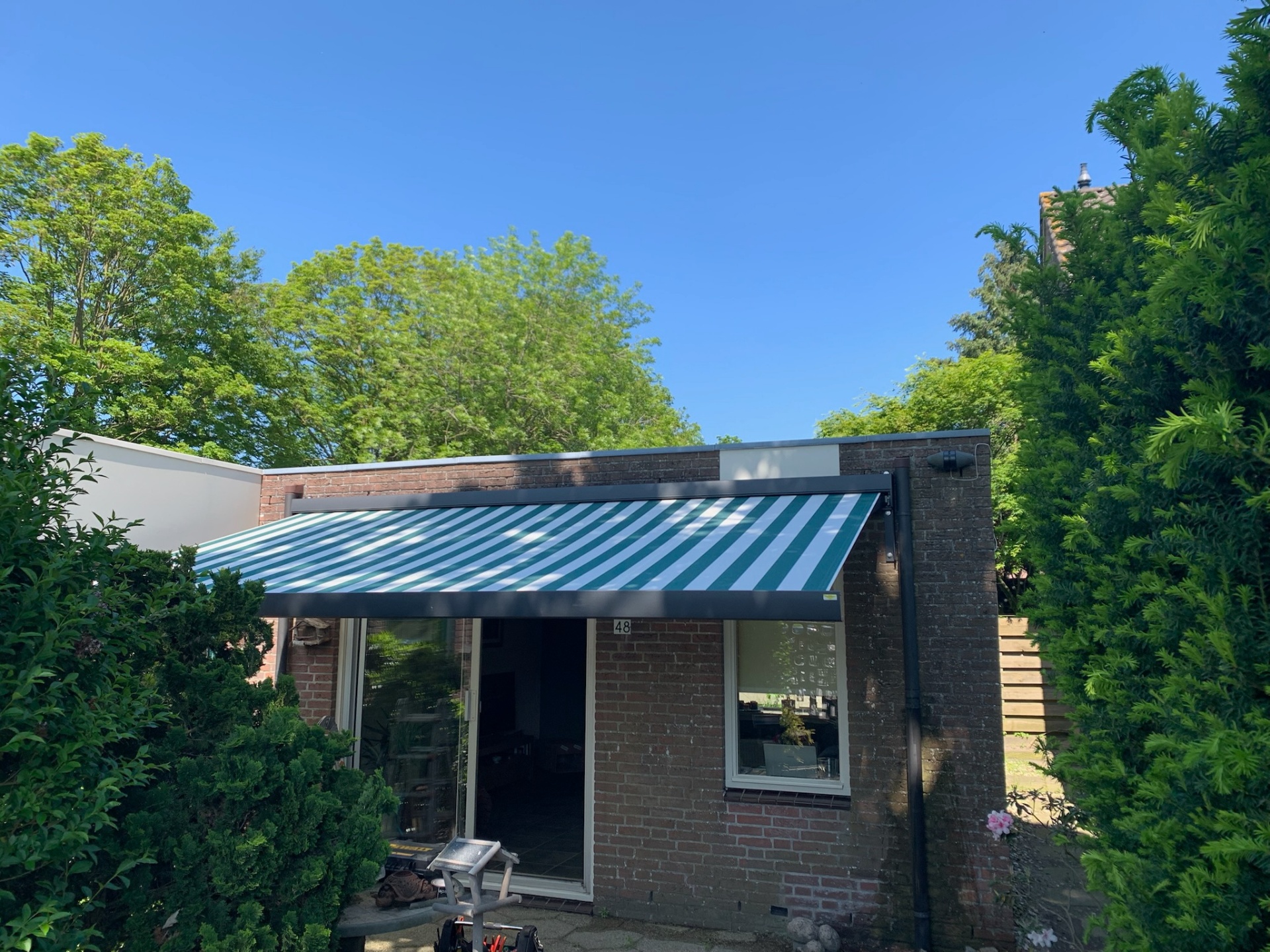 Knikarmscherm met groen-wit gestreept doek boven terras