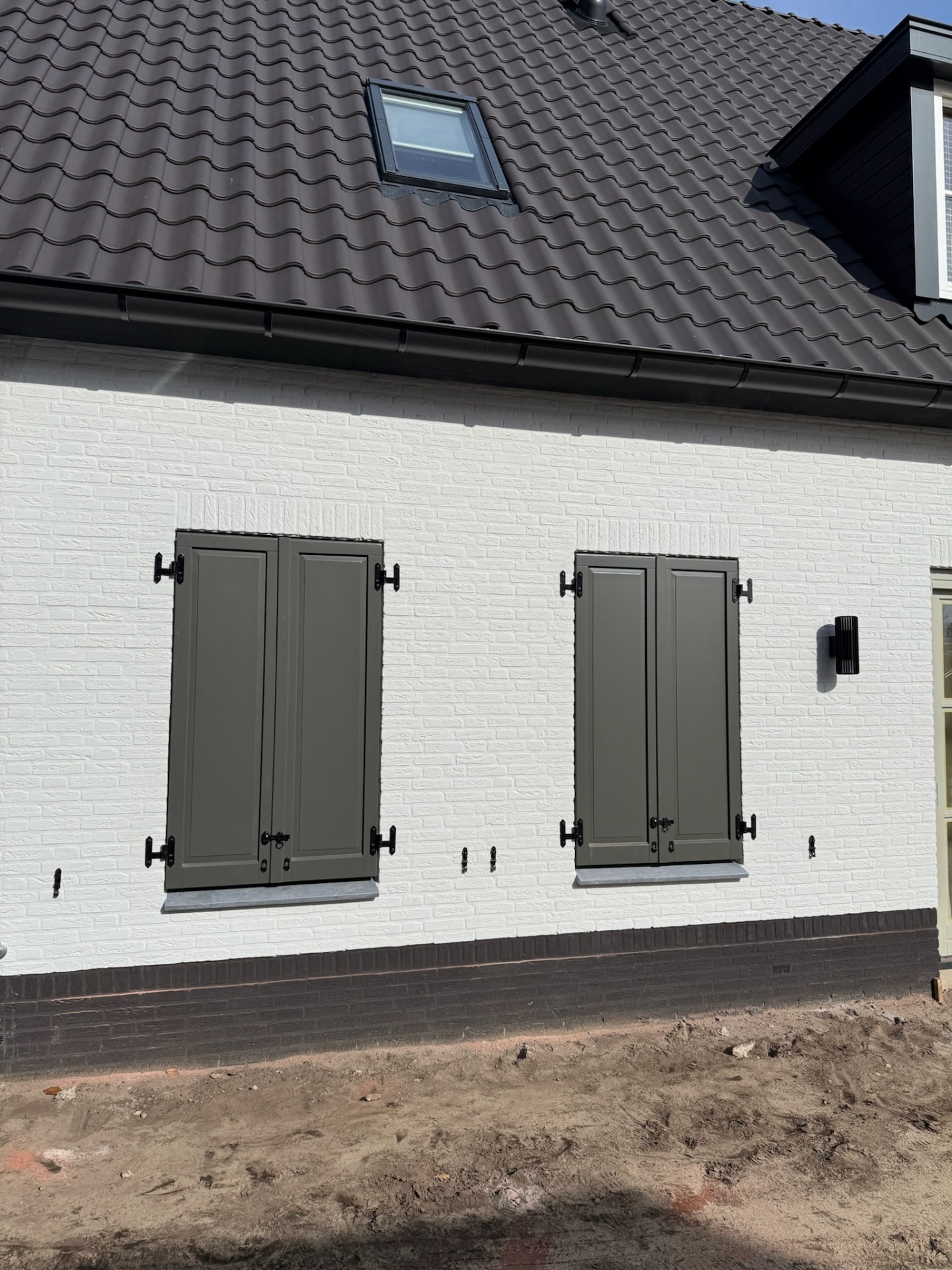 Olijfgroene luiken op witte gevel met smeedijzeren beslag