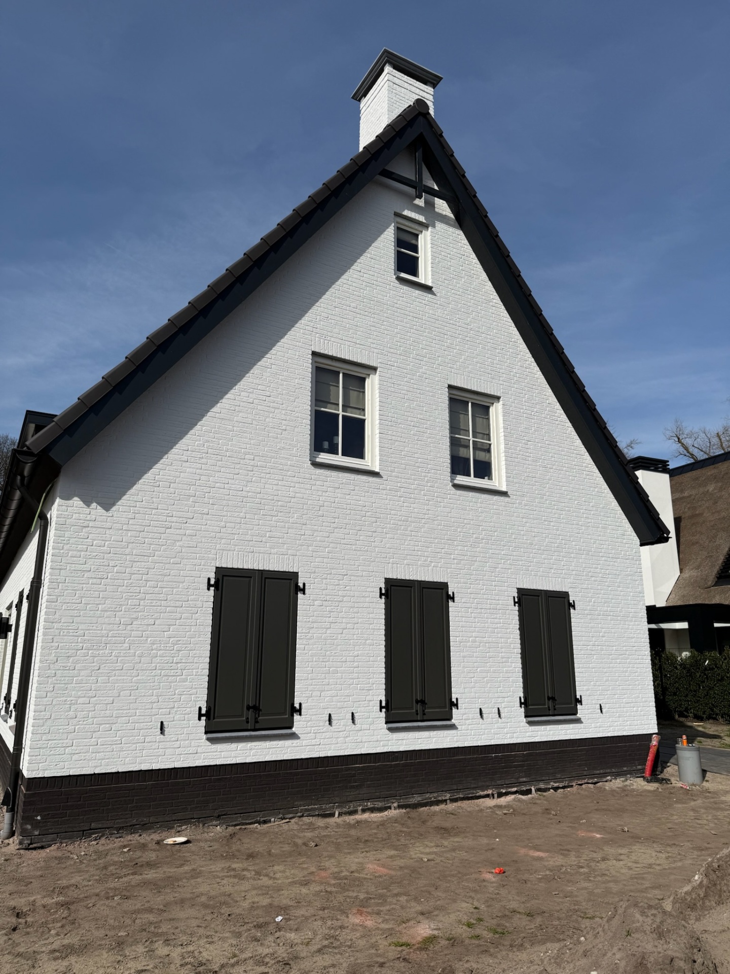 Antraciet houten luiken op witte bakstenen gevel met dakkapel