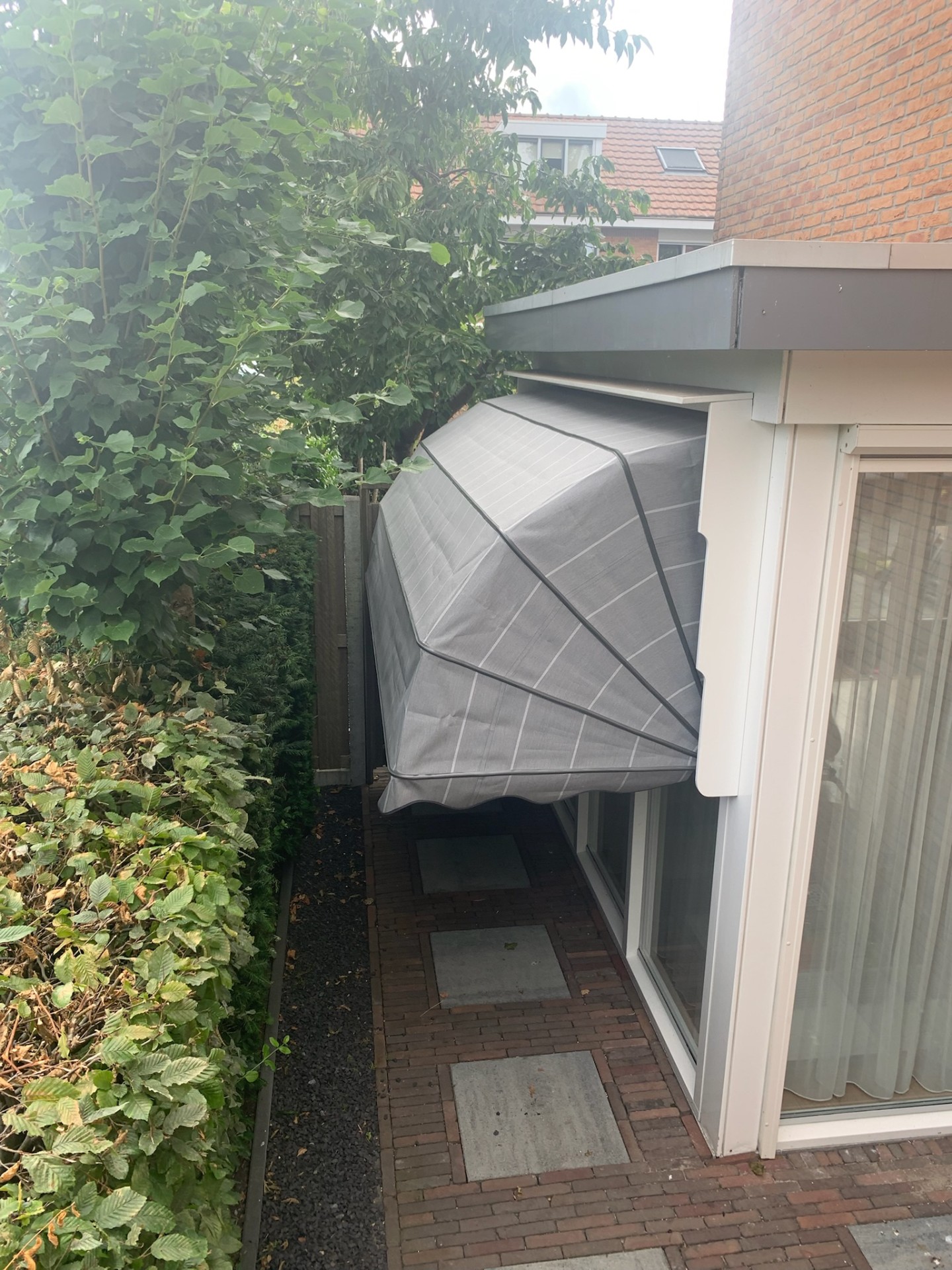 Grijs gestreepte markies aan zijgevel boven schuifpui