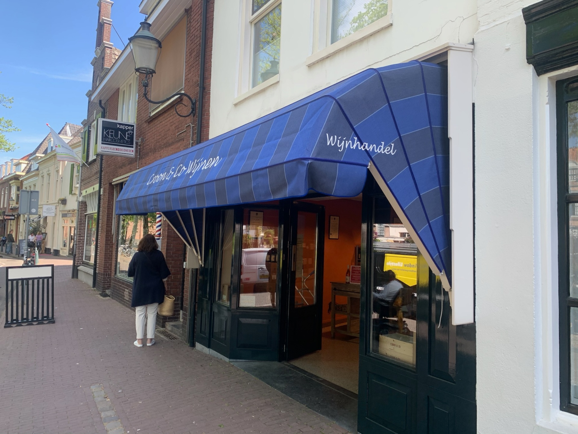 Blauw gestreepte markies met witte belettering boven wijnhandel in historisch centrum