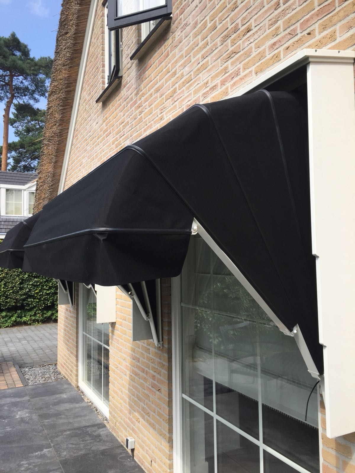 Zwarte markies met klassieke baleinen op villa met rieten dak