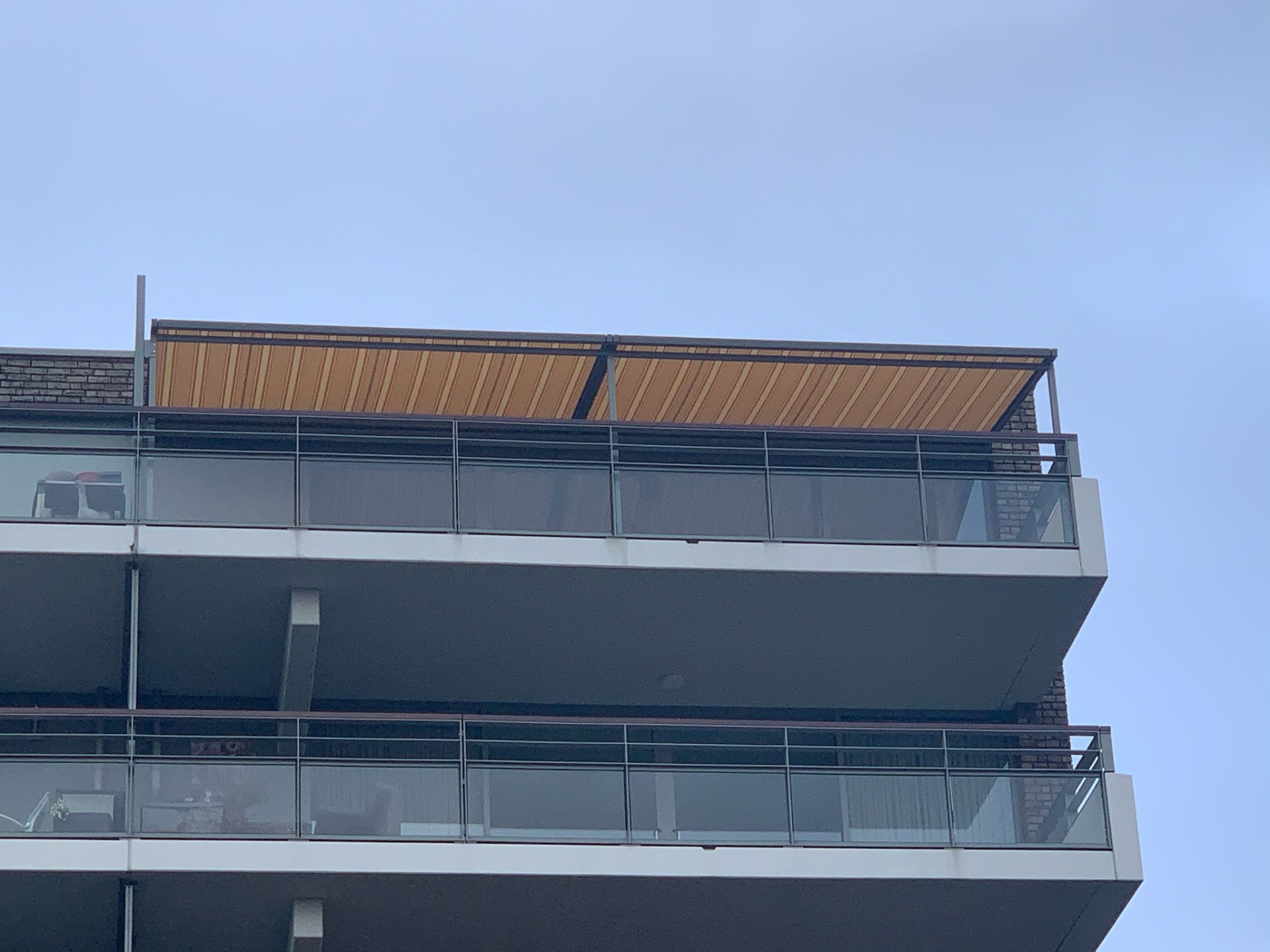 Pergola met geel-oranje doek op dakterras van appartementencomplex