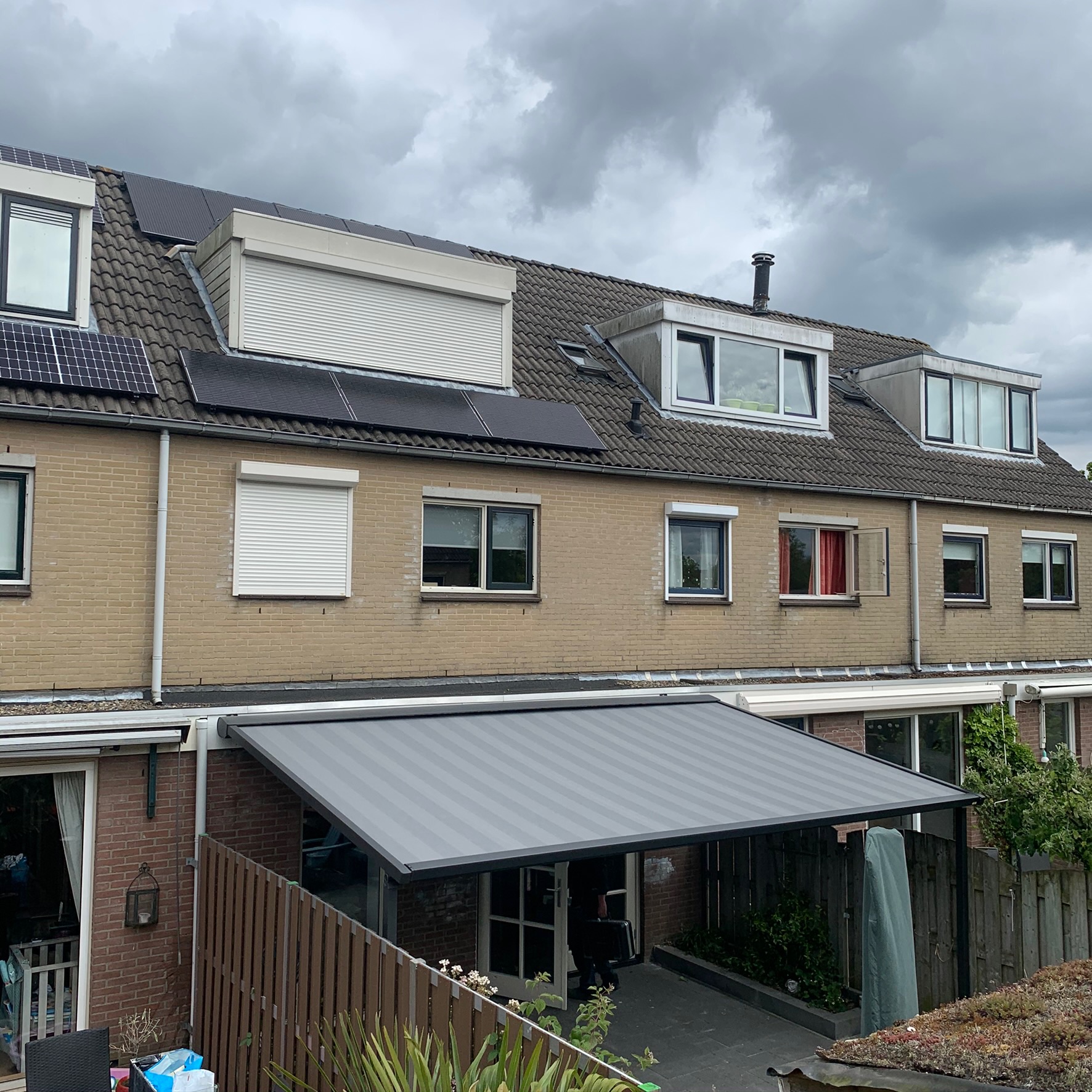 Pergola met grijs gestreept doek aan tussenwoning met dakkapel