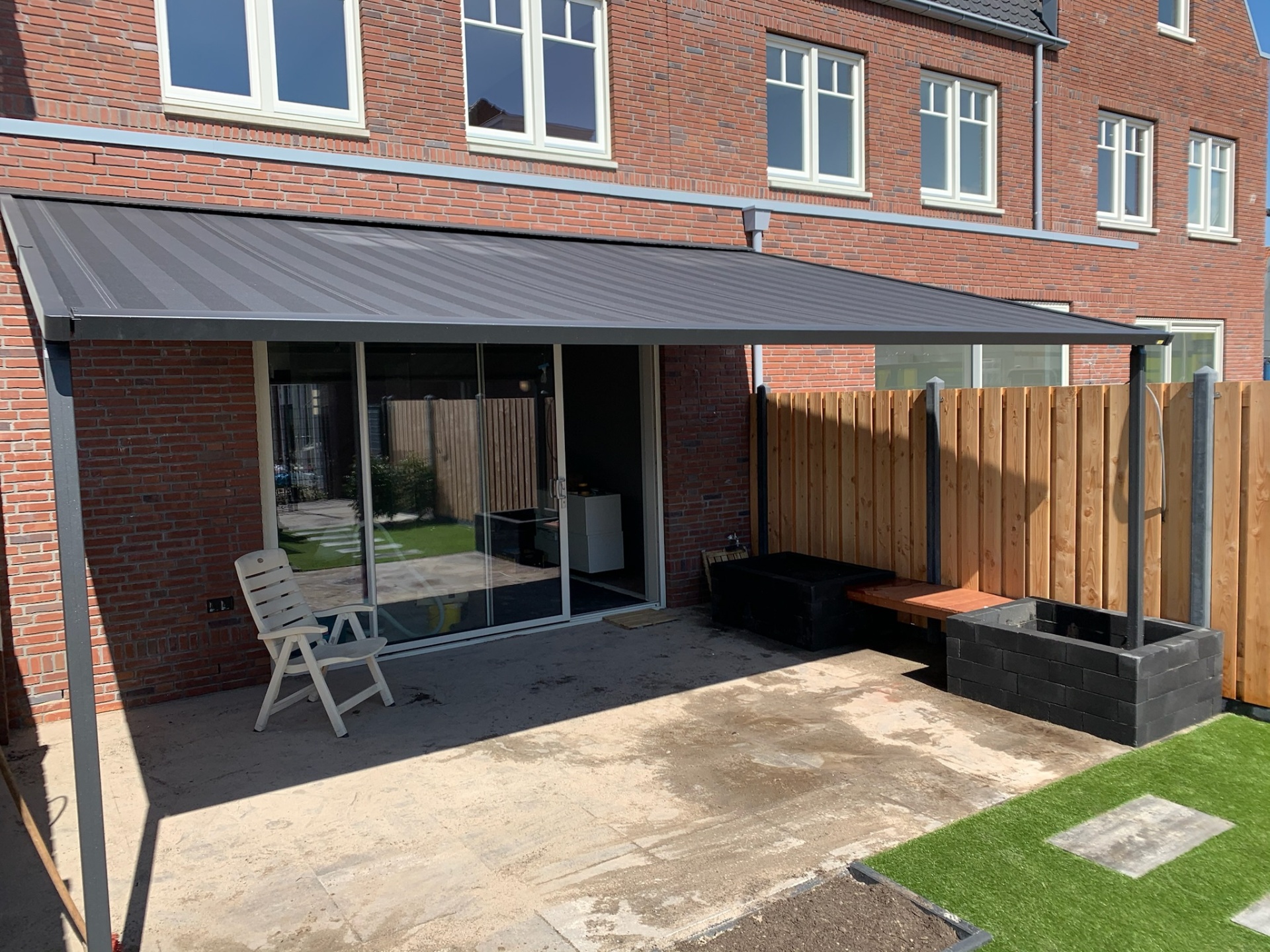 Pergola met antraciet doek aan moderne rode baksteen woning