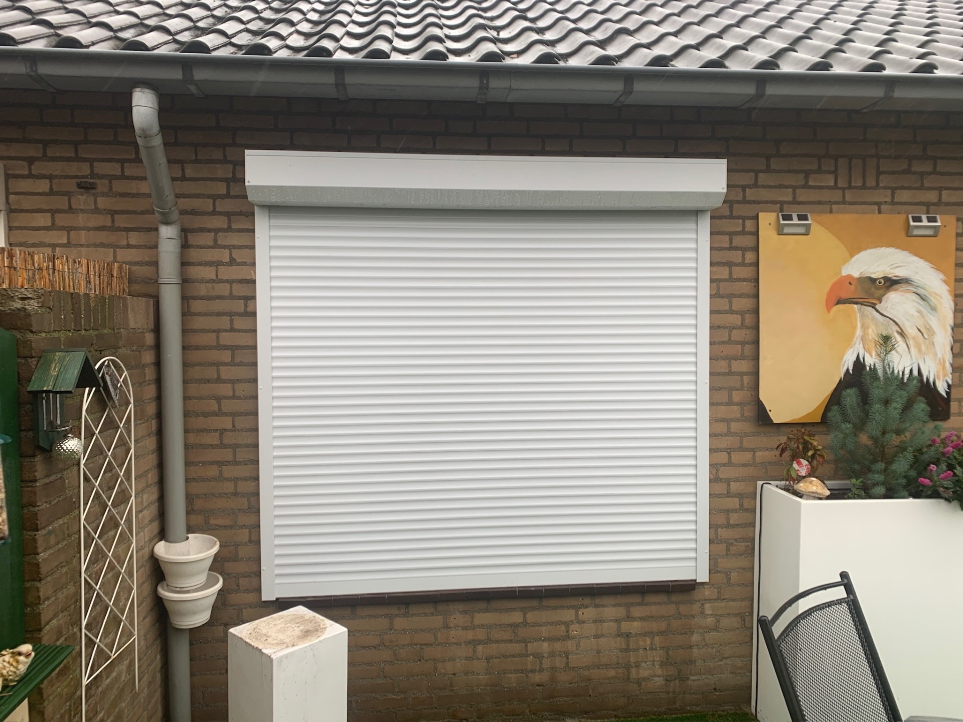 Wit rolluik op tuinraam van bungalow met regenpijp