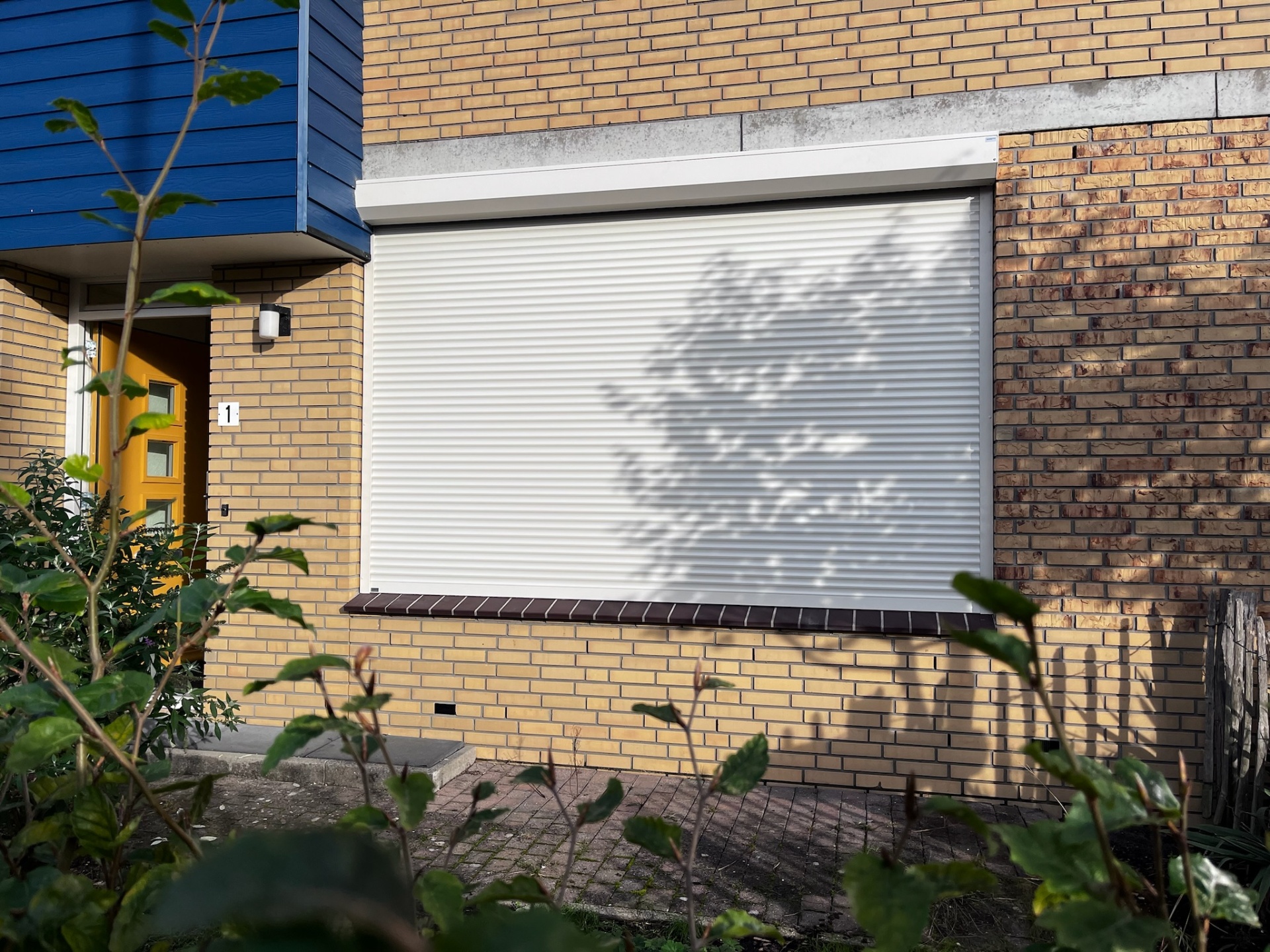 Wit rolluik op groot voorraam van moderne woning met gele baksteen