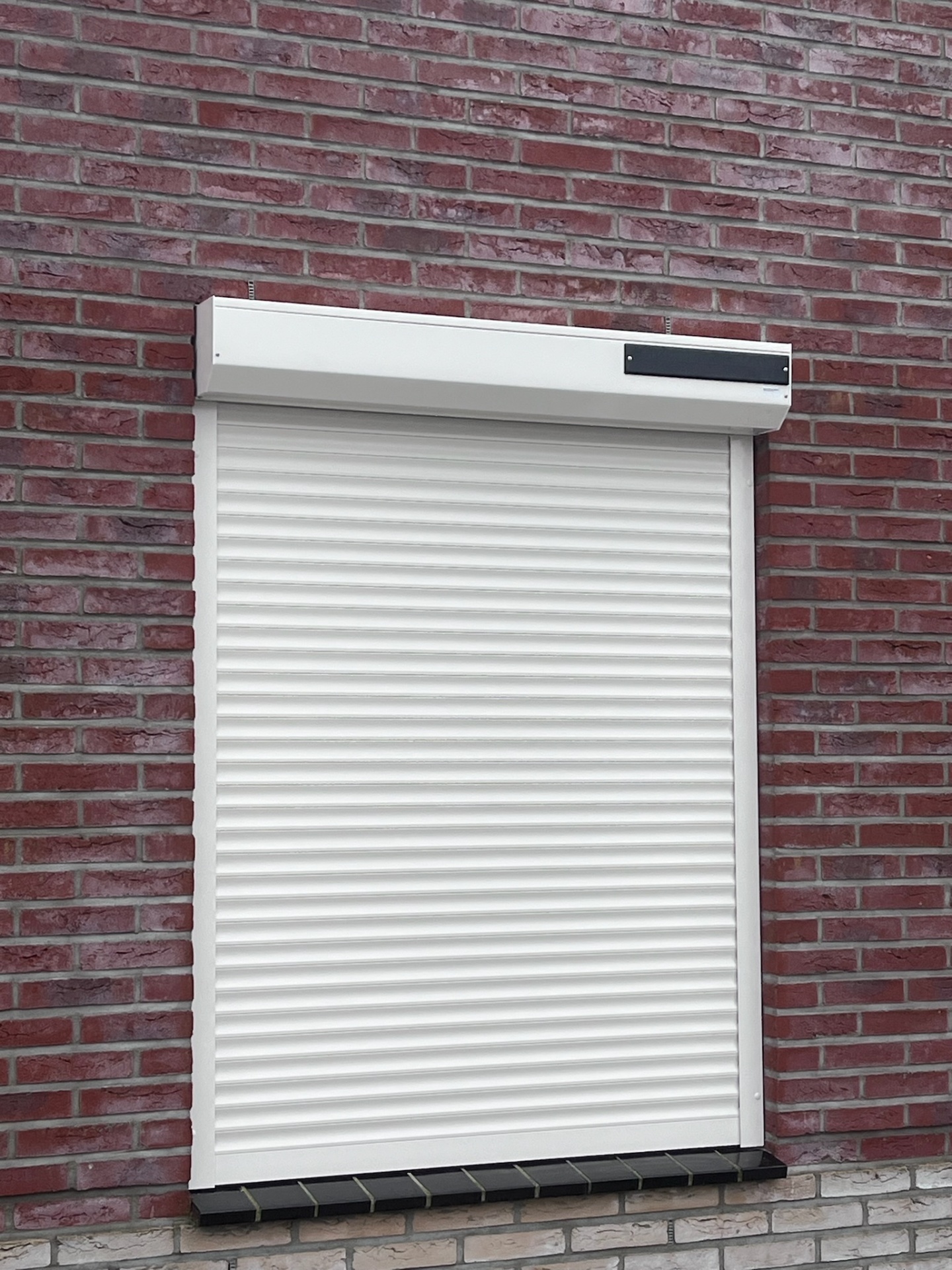 Wit opbouw-rolluik met zonne-energie module op rode bakstenen gevel