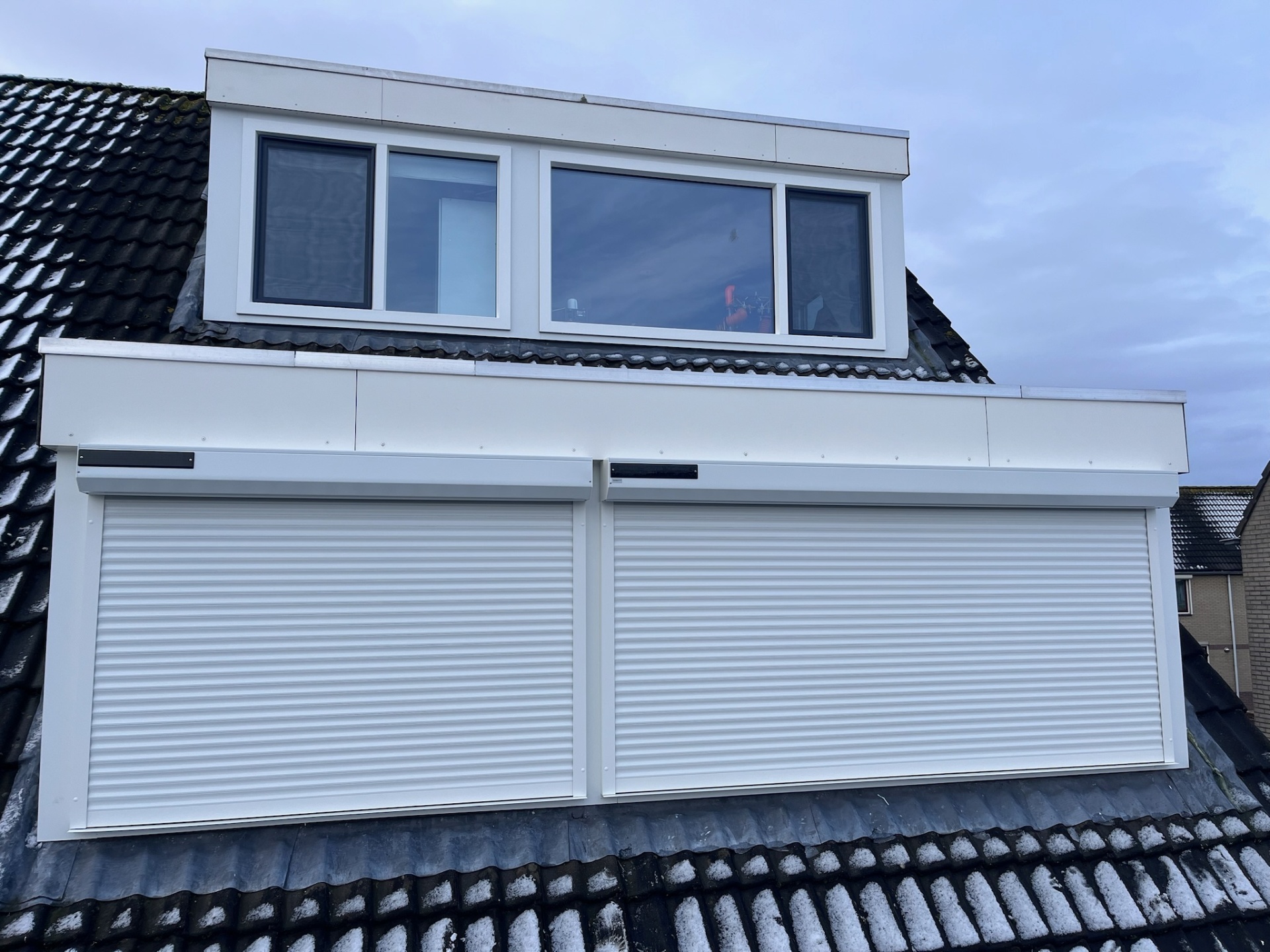 Twee witte solar-rolluiken op dakkapel met sneeuw op pannen
