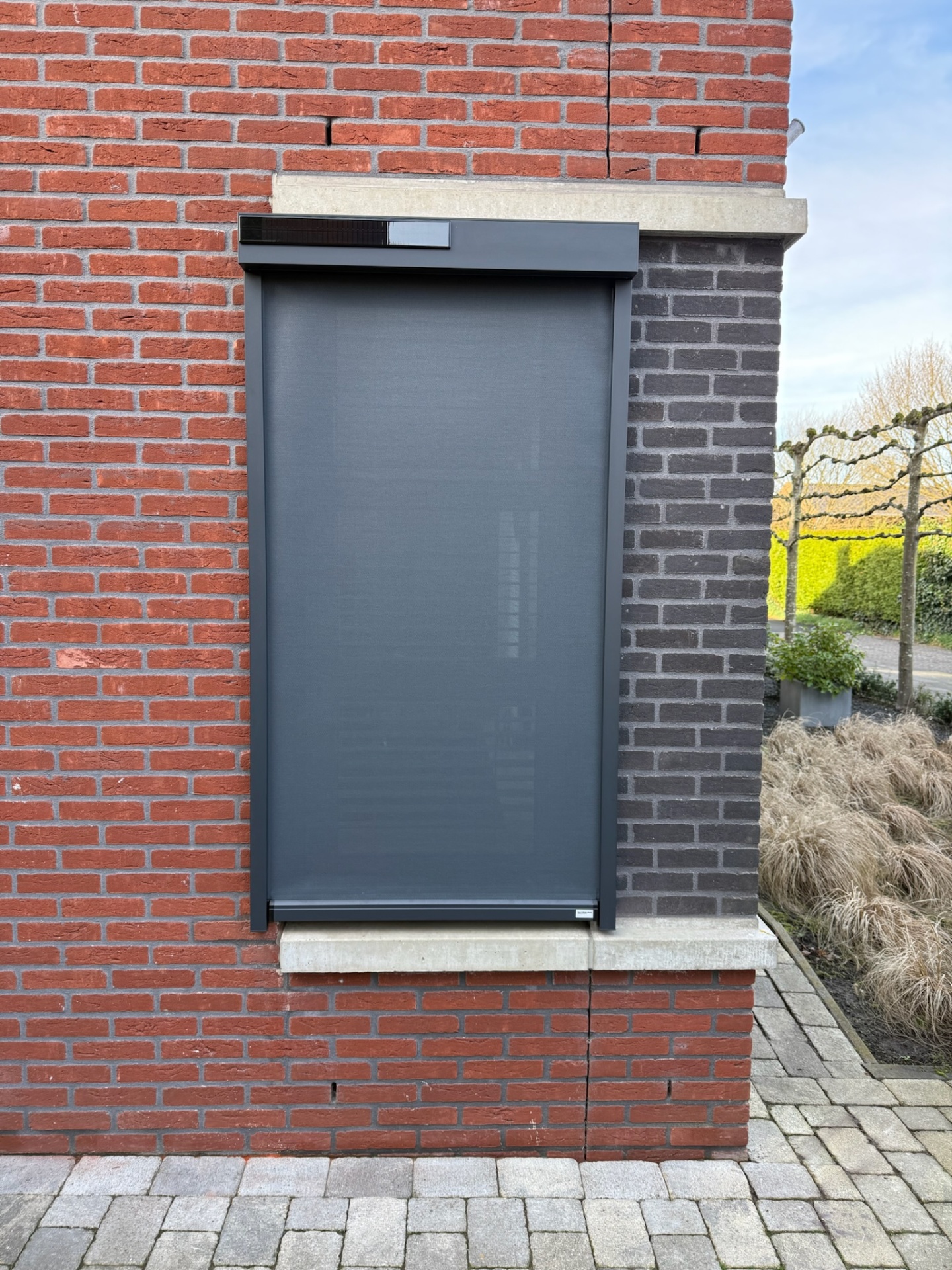 Antraciet zip-screen met geïntegreerde zonnecel op bakstenen gevel