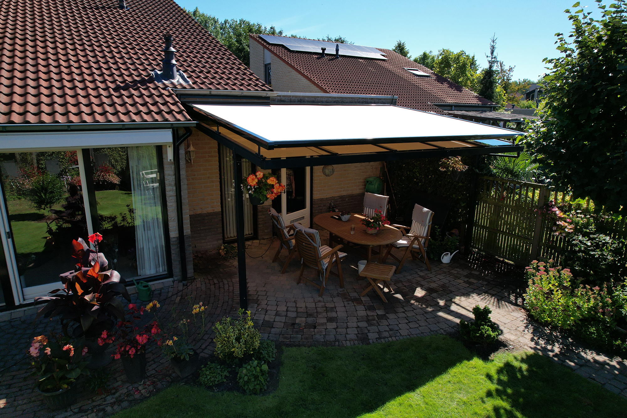 Witte serre zonwering boven patio aan woning met rood pannendak