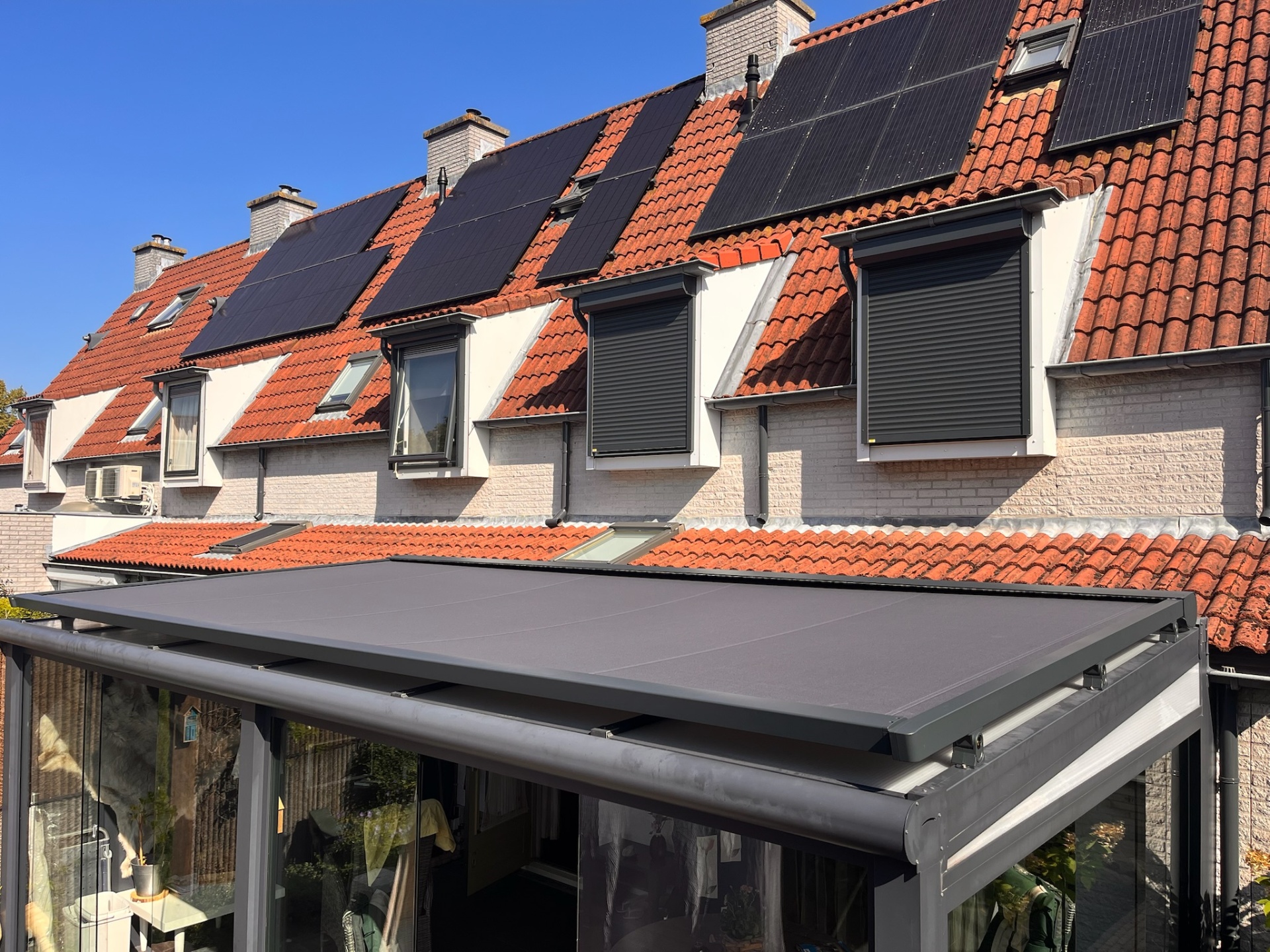Serre zonwering op glazen aanbouw onder dak met zonnepanelen en rolluiken