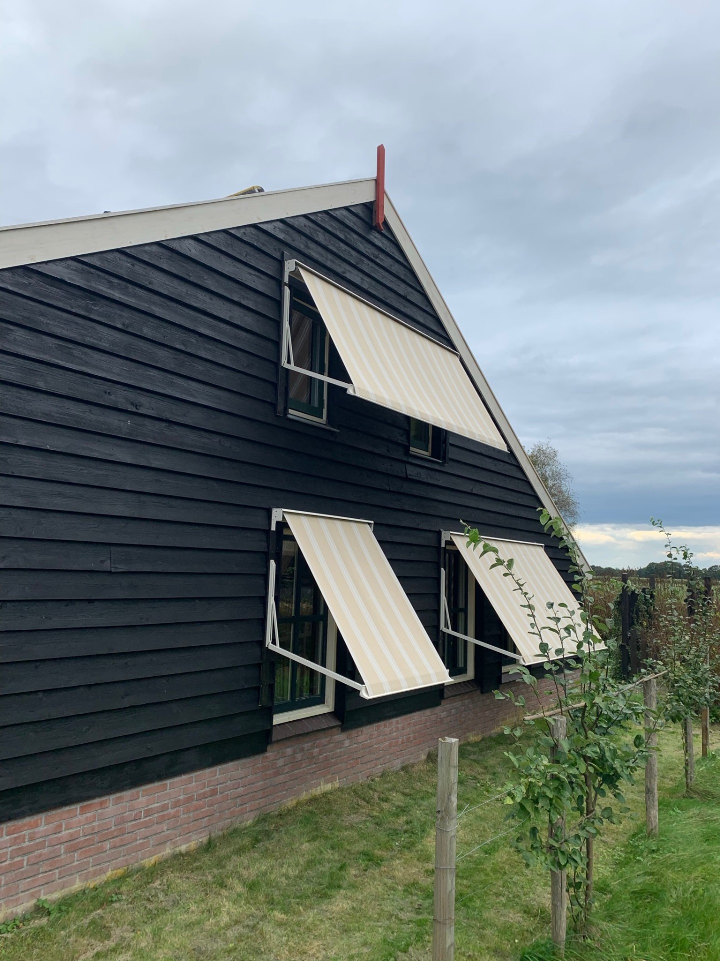 Drie uitvalschermen met crème gestreept doek op zwarte houten schuurwoning