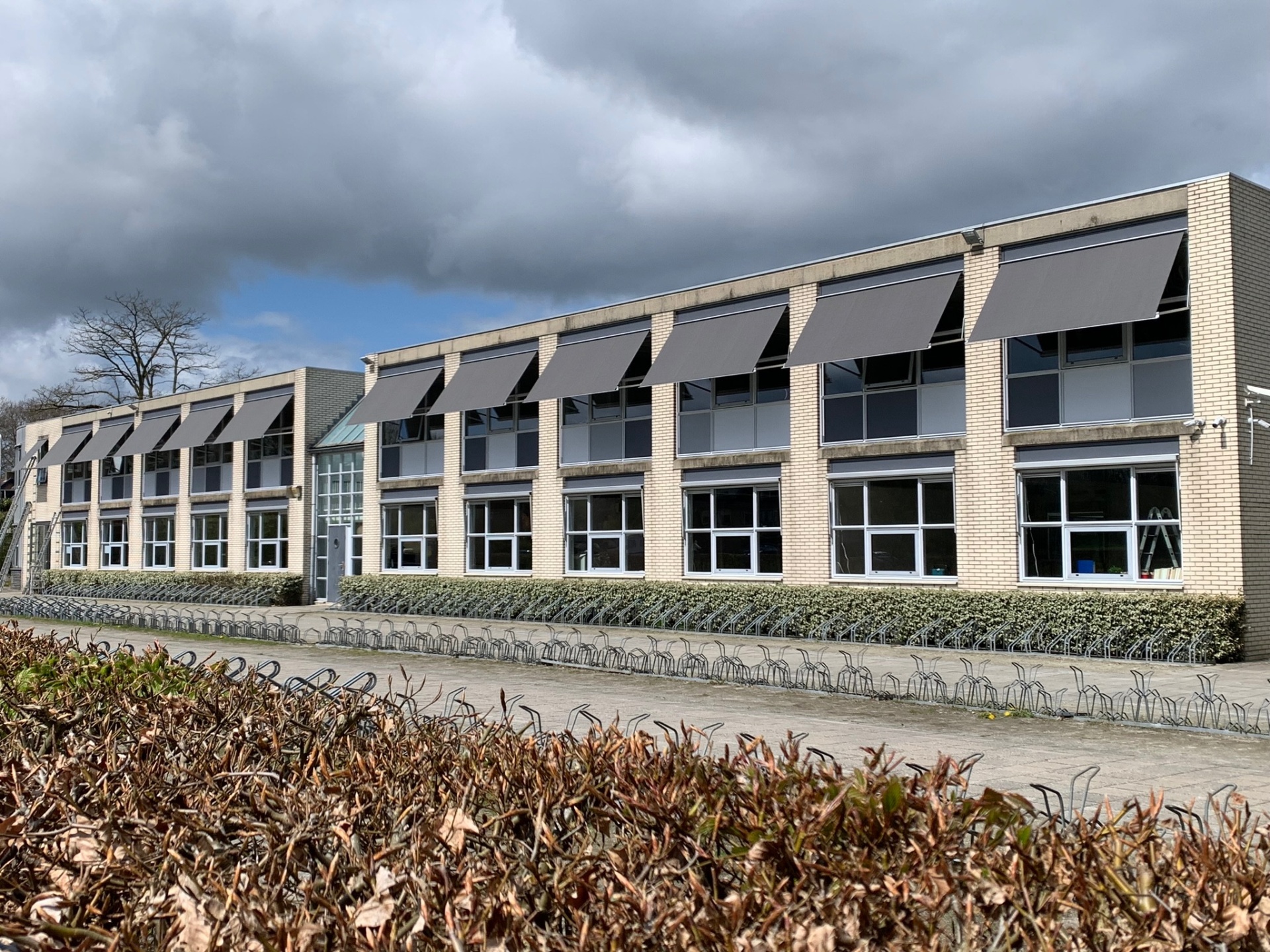 Lange rij grijze uitvalschermen op gevel van schoolgebouw